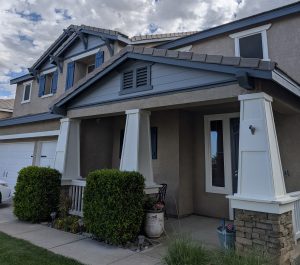 Close-up of a professional exterior paint job in Santa Clarita featuring blue shutters, white pillars, and tan stucco.