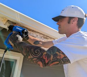Professional exterior painter Paint Daddy on a ladder using a heat gun to remove flaking paint during a detailed prep phase on a Santa Clarita home.