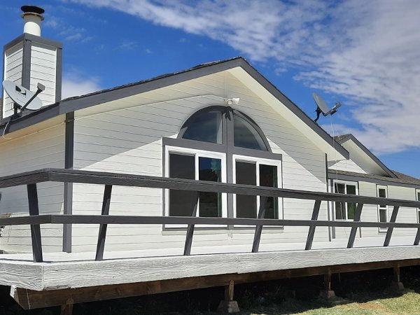 Full exterior view of an Action, CA ranch home featuring brilliant white siding, slate grey trim, and a massive wraparound deck by Paint Daddy.