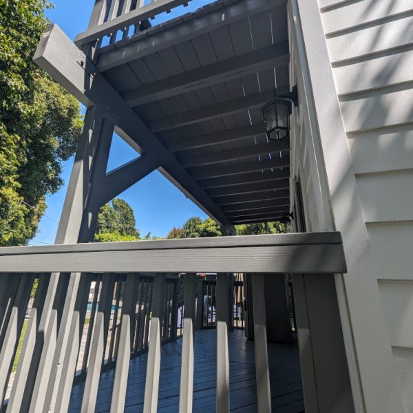 A professional view of a two-story wooden deck featuring slate grey structural supports, joists, and railings next to white lap siding by Paint Daddy.