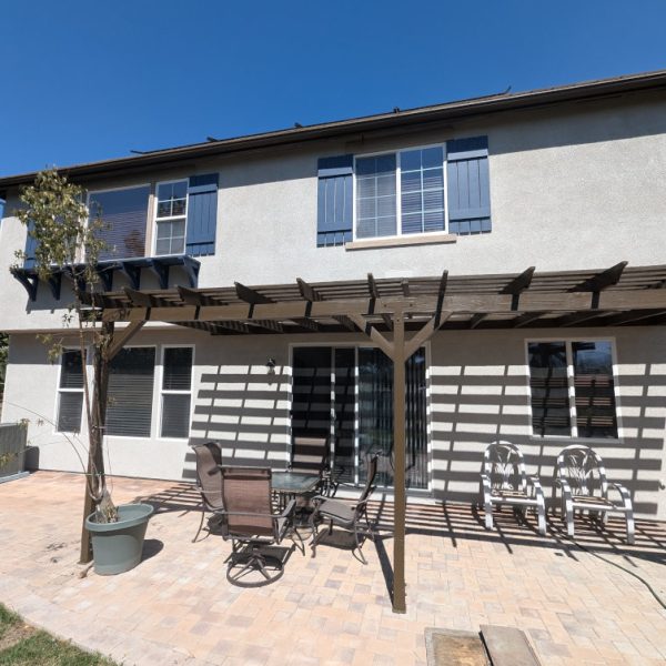 Rear elevation of a Santa Clarita home featuring a newly painted large wooden pergola with a deep espresso brown finish, matching all window trim and the new tan stucco exterior, by Paint Daddy.