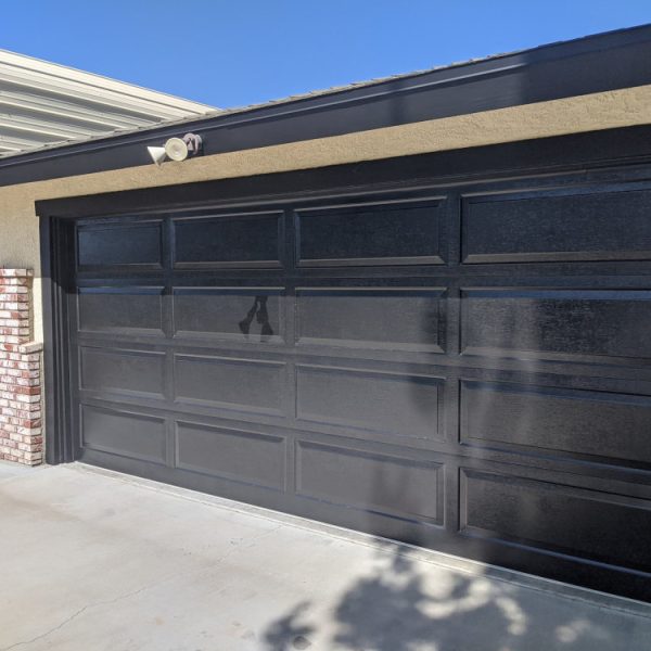 A multi-panel residential garage door in Littlerock freshly painted in a uniform semi-gloss black finish by Paint Daddy.