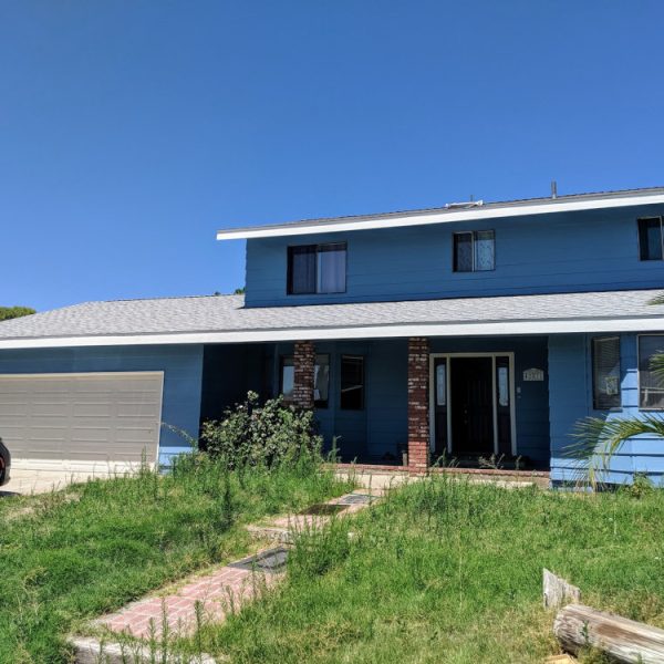 Full front view of a freshly painted two-story home in Lancaster, CA, featuring a vibrant blue body on horizontal lap siding and high-contrast crisp white trim on the fascia and roofline by Paint Daddy.