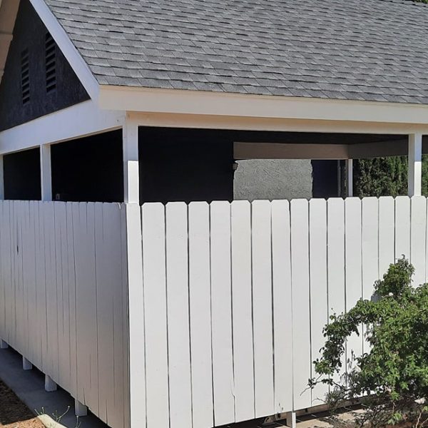 A modern gabled carport and residential exterior featuring deep charcoal stucco, brilliant white fascia, and matching white vertical fencing by Paint Daddy.