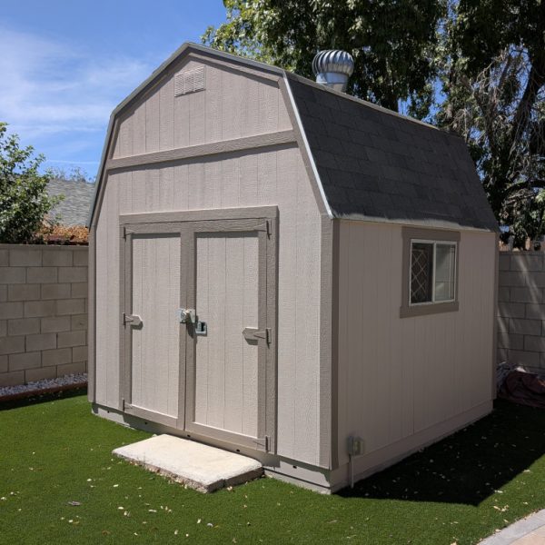 A gambrel-roof garden shed painted to match the main house in sandy tan with cocoa taupe trim and door accents by Paint Daddy.