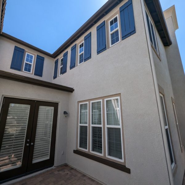 Detailed view of a residential courtyard in Santa Clarita featuring freshly painted tan stucco, navy blue shutters, and deep espresso brown French doors with tan trim accents, by Paint Daddy.