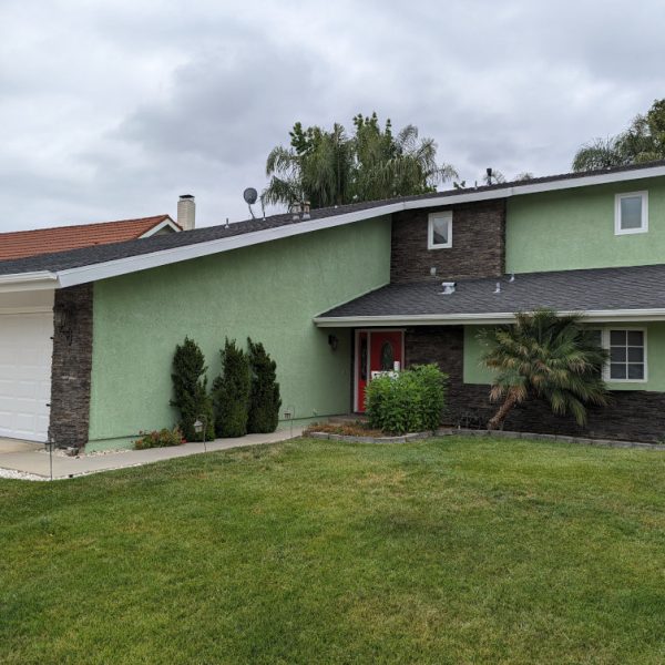 Full front elevation of a unique sage green residential exterior repaint in Santa Clarita, featuring crisp white trim and dark stone accents by Paint Daddy.