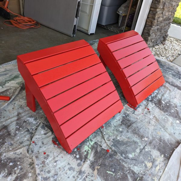 Two Adirondack chairs being repainted in a vibrant red finish on a professional drop cloth, showcasing the detail-oriented work of Paint Daddy.