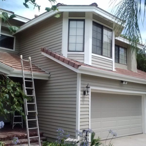 Full front elevation of a freshly repainted home in Santa Clarita featuring tan lap siding, crisp white trim, and matching garage doors, completed by Paint Daddy.