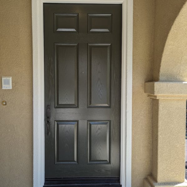 Close-up of a perfectly refinished high-gloss dark gray front door, with clean white trim contrasting against tan stucco, completed with second-generation detail by Paint Daddy in SCV.
