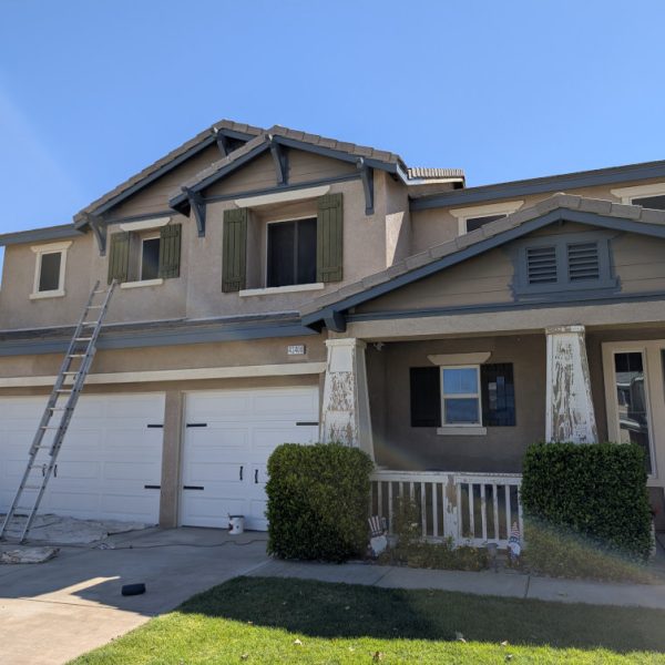 A professional in-progress exterior painting scene in Santa Clarita, CA, showing scraped pillars, drop cloths, and ladders over the front door of a home's entryway.