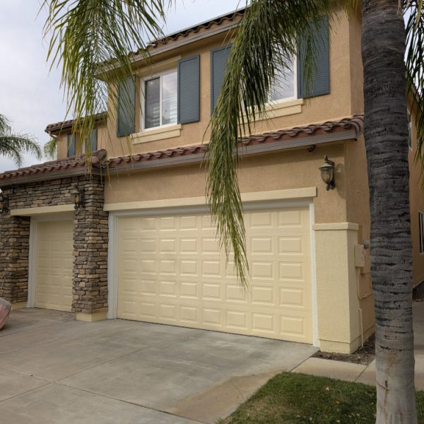 A professional residential exterior repaint in Santa Clarita, CA, featuring freshly painted cream garage doors, deep blue shutters, and crisp trim integrated with natural stonework by Paint Daddy.