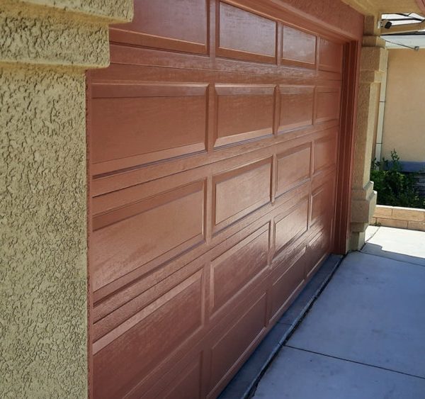 A profile view showing a freshly painted terracotta garage door with a uniform semi-gloss finish next to warm ochre textured stucco by Paint Daddy.