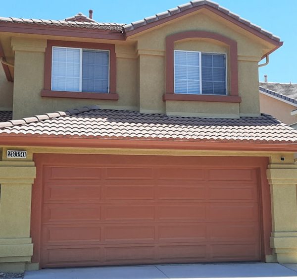 Full front elevation of a Mediterranean-style home featuring warm golden tan stucco, terracotta window trim, and a matching terracotta garage door by Paint Daddy.
