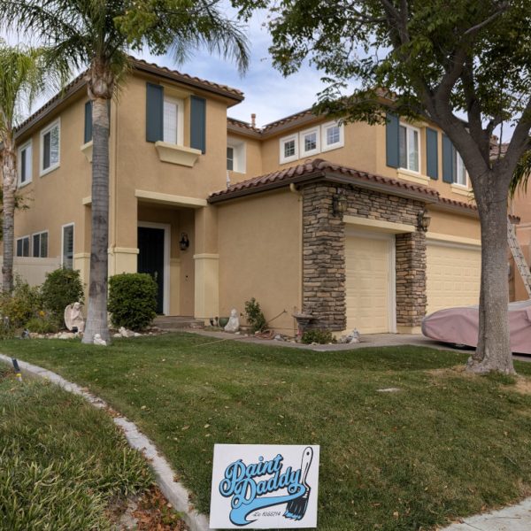Full front view of a complete residential stucco repaint in Santa Clarita, CA, featuring a yellow 'Paint Daddy' yard sign with professional landscaping, finished by licensed painter Paint Daddy.