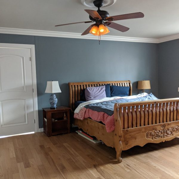 A professional interior painting job of a master bedroom in Santa Clarita, featuring a deep blue accent wall contrasting with crisp white crown molding and ceiling, completed by Paint Daddy.