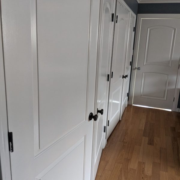 An interior hallway view from a full home repaint in Santa Clarita, CA, showing several freshly painted white paneled doors and casings against new gray walls and wood floors by Paint Daddy.