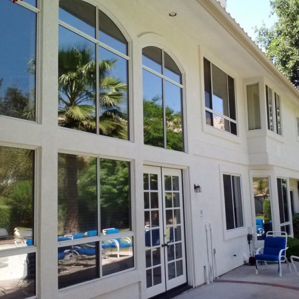 Rear elevation of a luxury white home in Valencia, CA, featuring freshly painted French doors and intricate window trim with palm tree reflections, completed by Paint Daddy.