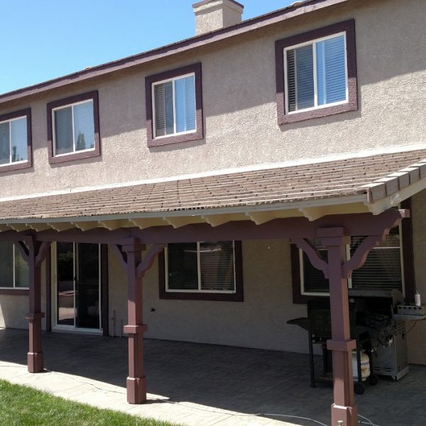 Rear view of a Lancaster residence showing a large wooden patio cover refinished in deep burgundy with matching window trim and taupe stucco by Paint Daddy.