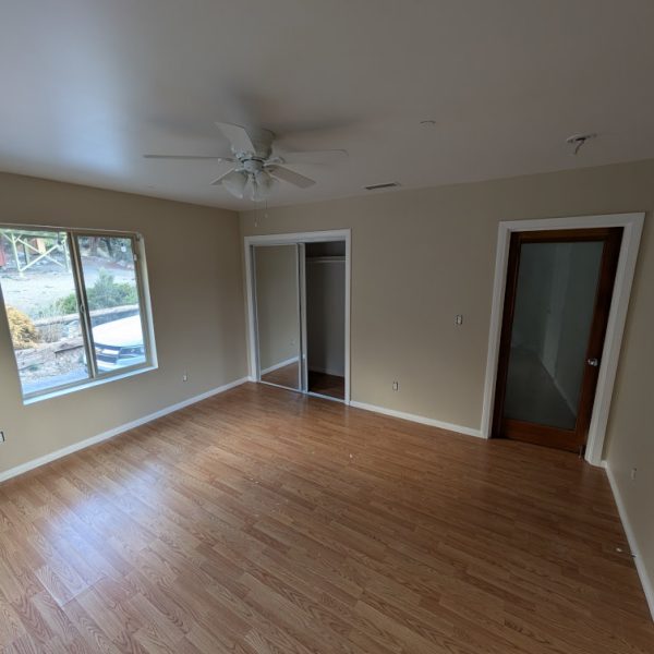 A large master bedroom featuring a professional tan wall finish and crisp white trim on windows and closet sliders, completed by Paint Daddy in Santa Clarita.