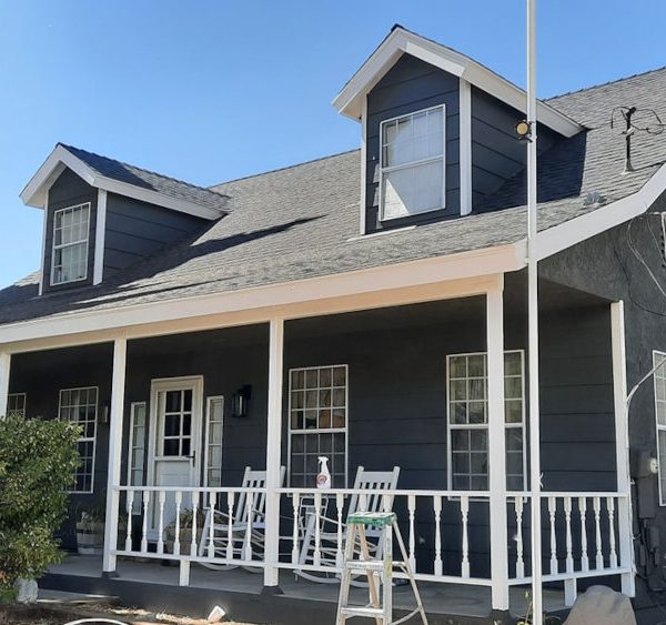 Full view of a two-story farmhouse-style home featuring deep slate charcoal siding and stucco with a high-contrast white porch and railing by Paint Daddy.