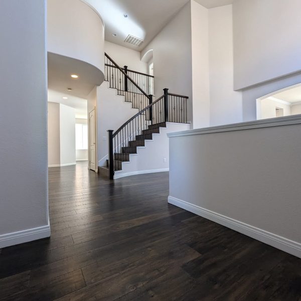 A detailed view of a grand staircase featuring espresso-stained handrails and white risers against neutral walls and dark wood flooring by Paint Daddy.