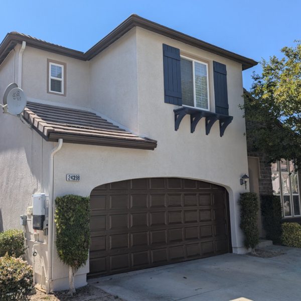 A professional full exterior repaint of a Santa Clarita home, featuring freshly applied tan stucco, navy blue shutters, and espresso brown trim on all fascia and garage doors by Paint Daddy.