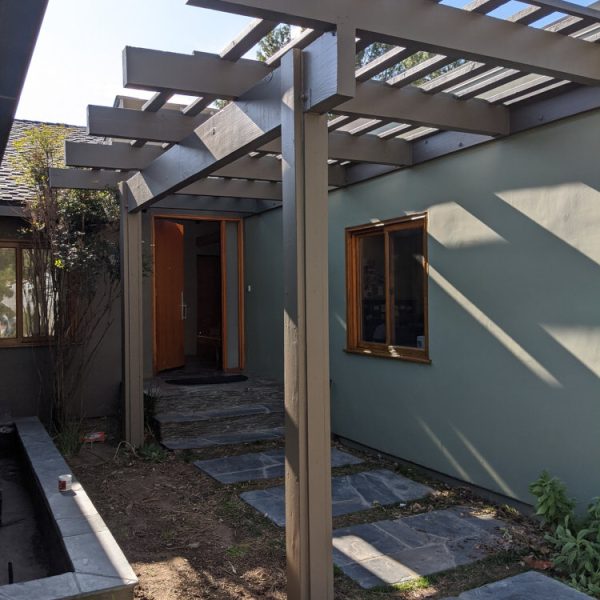 A modern home entryway featuring sage green stucco walls and a dark bronze architectural pergola by Paint Daddy.