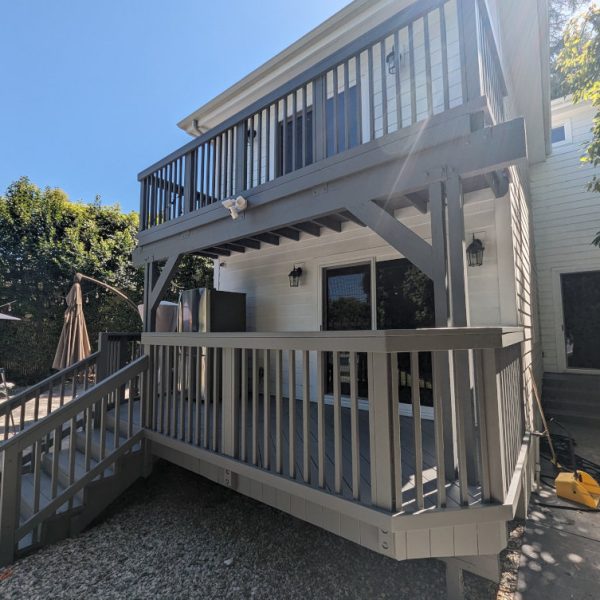 A full view of a finished multi-level backyard deck in Santa Clarita, featuring a professional grey finish on all railings, stairs, and support beams against original white siding, by Paint Daddy.