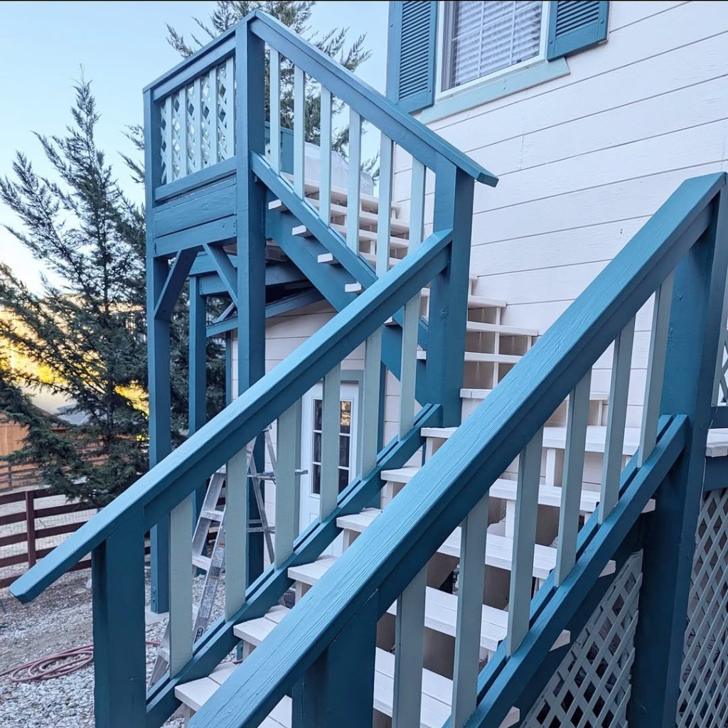 A massive multi-landing exterior wooden staircase painted in teal and sage green with off-white treads by Paint Daddy.