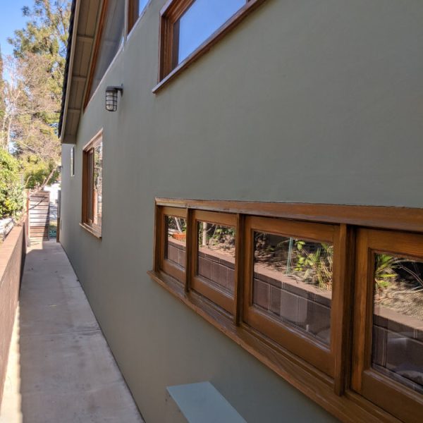 Close-up profile of a sage green stucco wall with natural wood window casings, showcasing sharp paint lines by Paint Daddy.