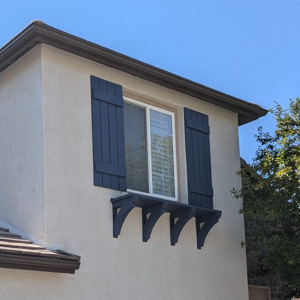 A detailed close-up of a decorative window shutter freshly painted in deep navy blue, set against newly applied tan stucco on a Santa Clarita home by Paint Daddy, showcasing clean lines and no overspray.