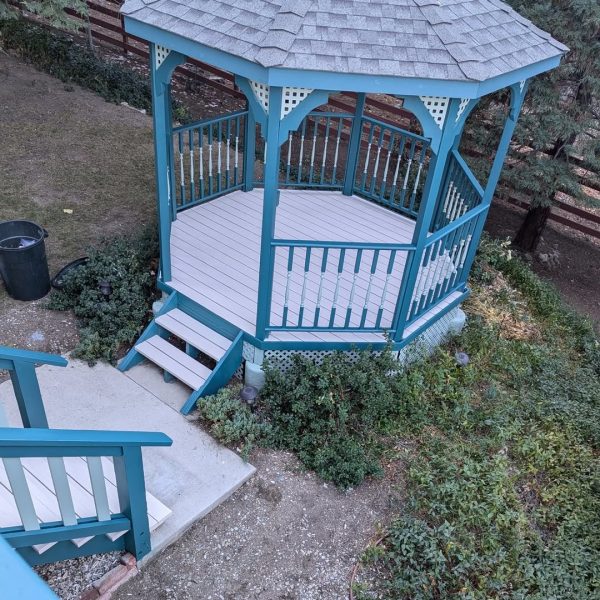 A fully restored octagonal garden gazebo featuring teal structural beams, sage green spindles and lattice, and an off-white floor and ceiling by Paint Daddy.