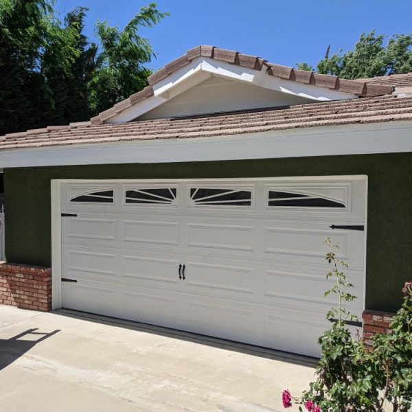 A residential garage featuring olive green stucco, red brick accents, and a brilliant white carriage-style garage door by Paint Daddy.