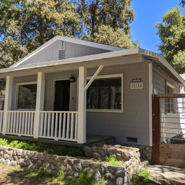 A cottage-style home featuring cool grey lap siding and a brilliant white porch on a river rock foundation by Paint Daddy.