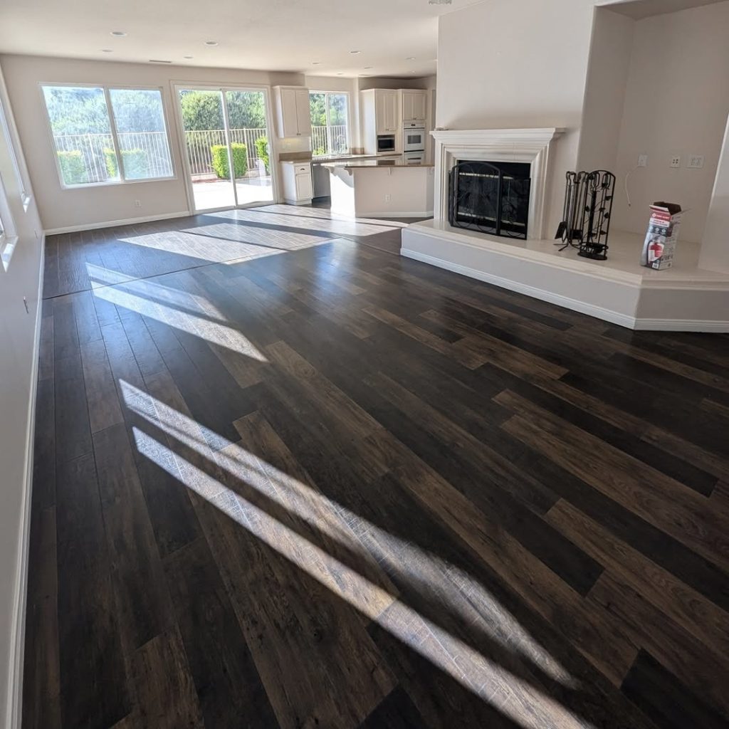 An open-concept living area in Valencia featuring a white mantel, dark wood floors, and matching white kitchen cabinetry by Paint Daddy.