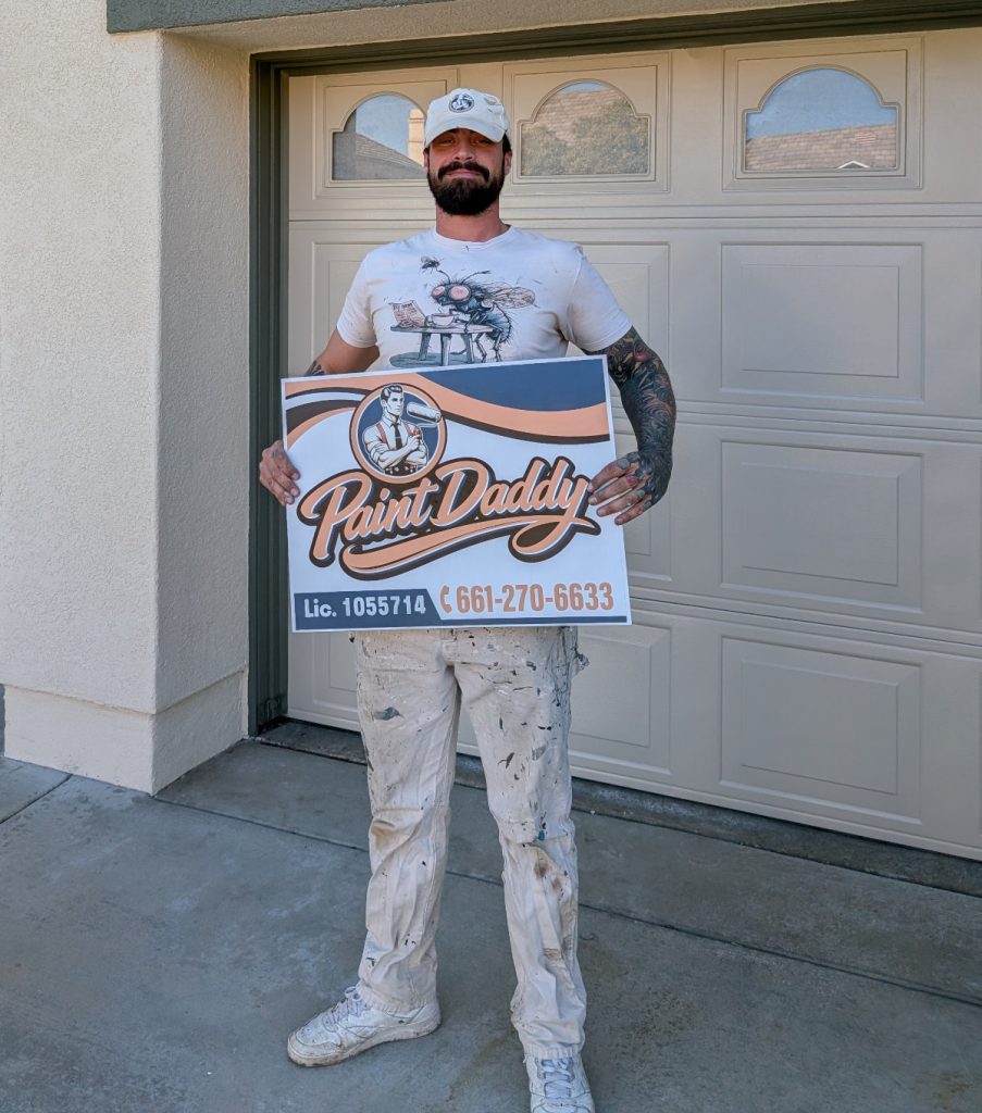 Professional painter Jake Griffus holding a Paint Daddy sign in front of a newly painted home.