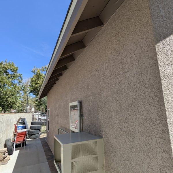 A sharp-angle profile view of a sandy tan stucco wall and cocoa taupe rafter tails and fascia, showcasing clean paint lines by Paint Daddy.