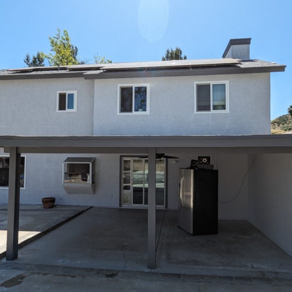 Rear elevation of a Lancaster home featuring a freshly painted dark grey patio cover and matching second-story window trim against clean white stucco, completed by Paint Daddy.