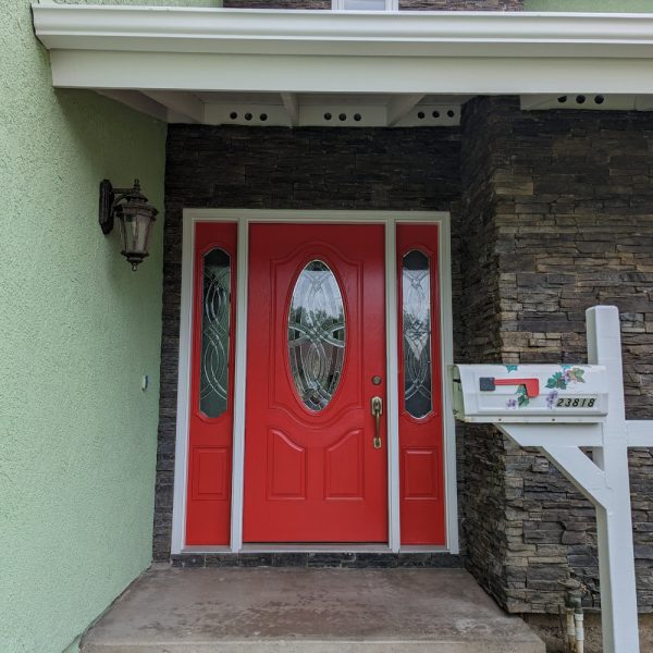 A vibrant red front door with detailed glass inserts, framed by crisp white trim and dark stacked stone, completed by Paint Daddy in Santa Clarita.