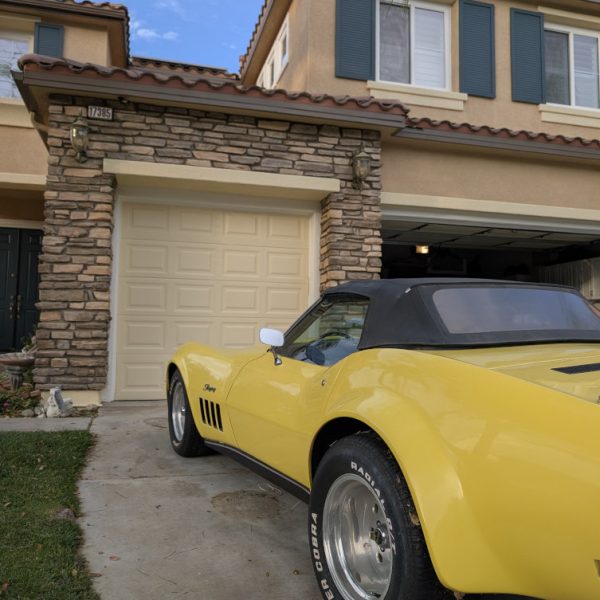 A yellow classic Corvette parked in front of a freshly repainted Santa Clarita home, highlighting the clean cream garage door and expert stonework integration by Paint Daddy.
