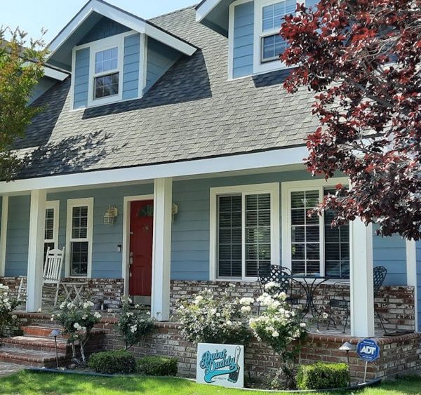 Full front elevation of a large residence featuring sky blue siding, a deep red entry door, and white columns on a brick foundation by Paint Daddy.