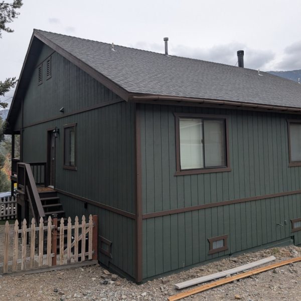 A freshly finished mountain cabin in Pine Mountain Club, CA, featuring forest green solid body stain on vertical siding with deep brown trim accents, by Paint Daddy.