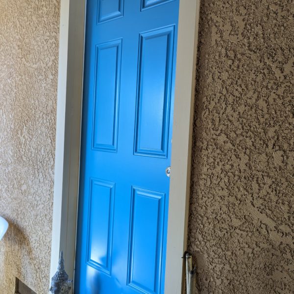 A professional close-up of a freshly painted turquoise entry door with a smooth semi-gloss finish, framed by tan trim and vibrant orange stucco on a Leona Valley ranch house, by Paint Daddy.