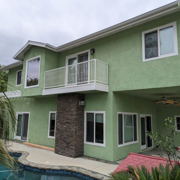 Backyard view of a two-story sage green home, showing freshly painted white balcony railings and window trim by Paint Daddy in Santa Clarita.