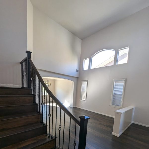 A grand Valencia living room featuring double-height neutral walls, dark walnut wood floors, and a modern black and white staircase by Paint Daddy.