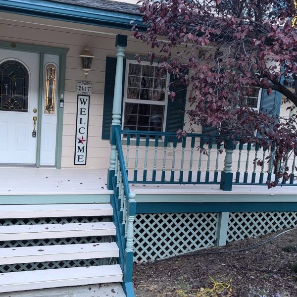 A Victorian-style front porch featuring teal railings and shutters, sage green spindles, and an off-white deck floor by Paint Daddy.