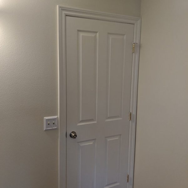 A freshly painted white 6-panel interior door and decorative casing with a smooth semi-gloss finish, showcasing clean lines against neutral walls by Paint Daddy.