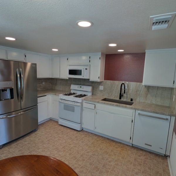 A professional kitchen cabinet transformation in Santa Clarita, CA, featuring a smooth white semi-gloss finish on upper and lower cabinets and a bold burgundy accent wall by Paint Daddy.