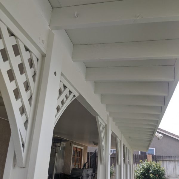 Underside view of a large wooden patio cover featuring intricate lattice fretwork and rafters freshly painted in brilliant white by Paint Daddy.